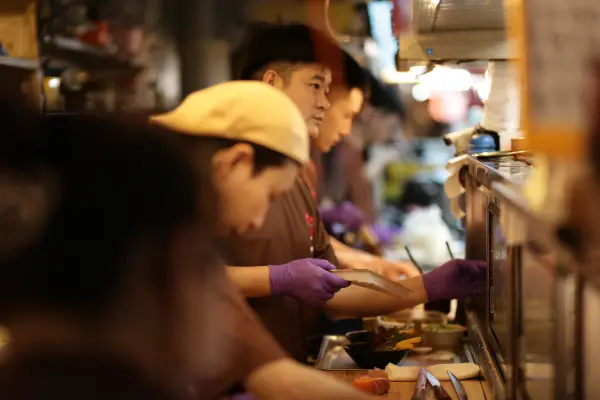 Kitchen workers preparing food along a busy service counter.