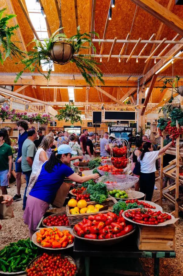 People moving among produce stands inside a busy food market.
