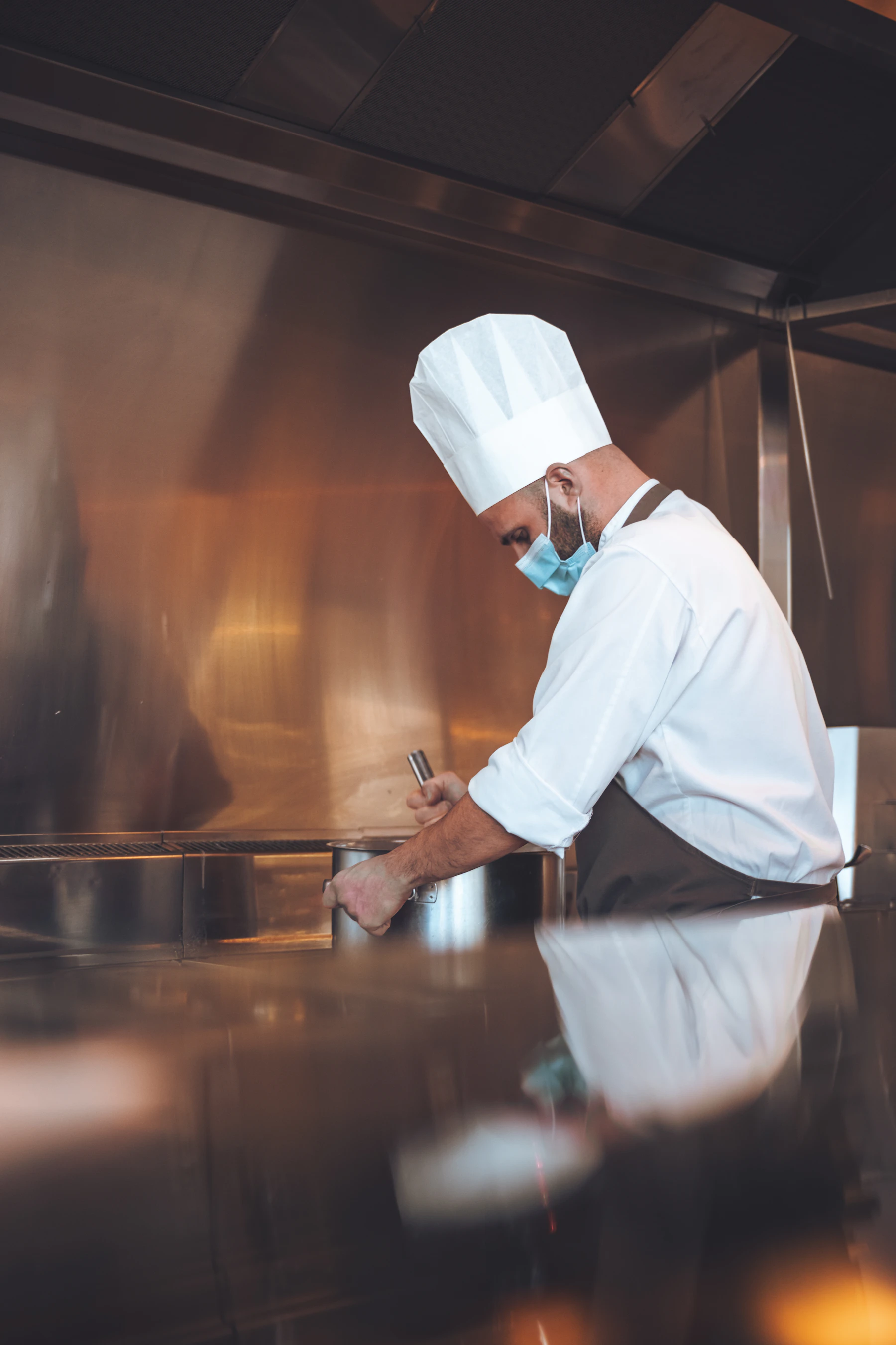 A chef stirring a large pot in a professional kitchen.